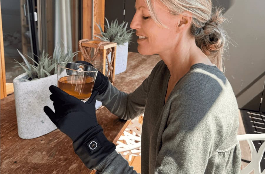 Frau mit beheizten Innenhandschuhen und einer Tasse Tee in den Händen