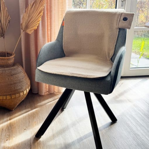 Beige elektrisch verwarmd stoelkussen van HeatPerformance® op een stoel bij het raam, voor heerlijk warme zithouding.