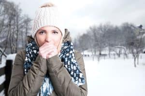 Vrouw heeft het koud in de sneeuw en blaast op haar handen.