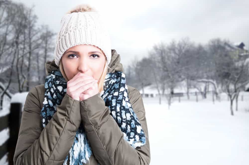 Vrouw heeft het koud in de sneeuw en blaast op haar handen.