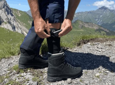 Un homme enfile des chaussettes chauffantes à piles sur un sentier de montagne